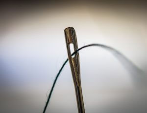 Close up photo of a thread passing through the eye of a needle