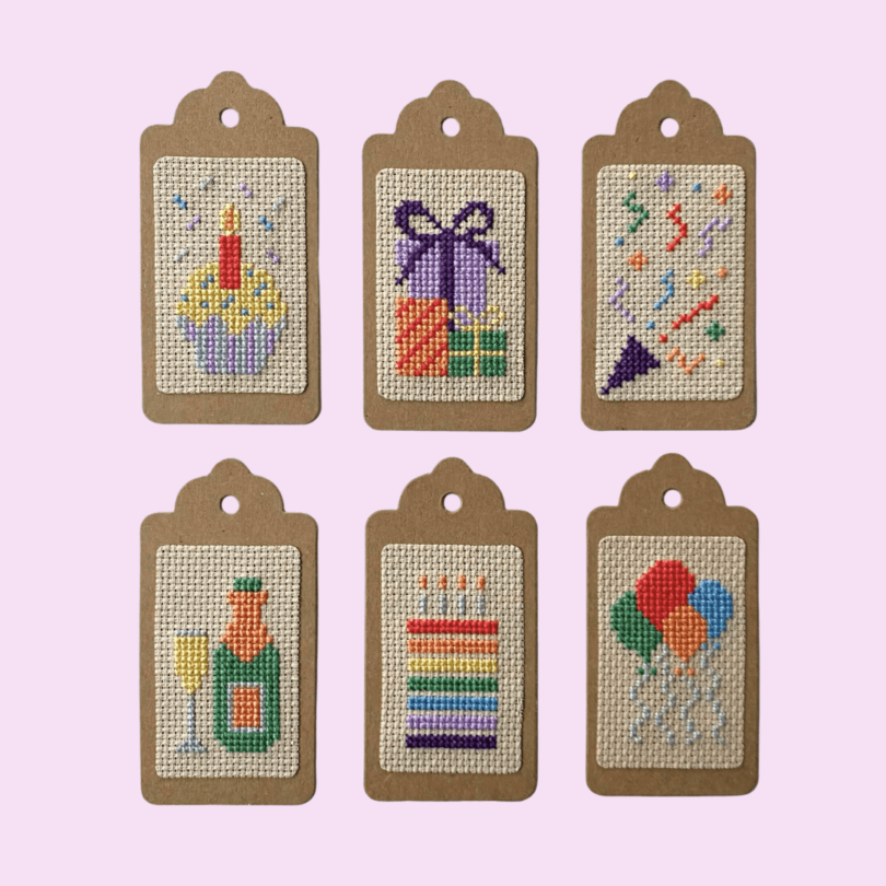 6 birthday cross stitched gift tags in different designs: cupcake, presents, streamer, champagne, cake and balloons